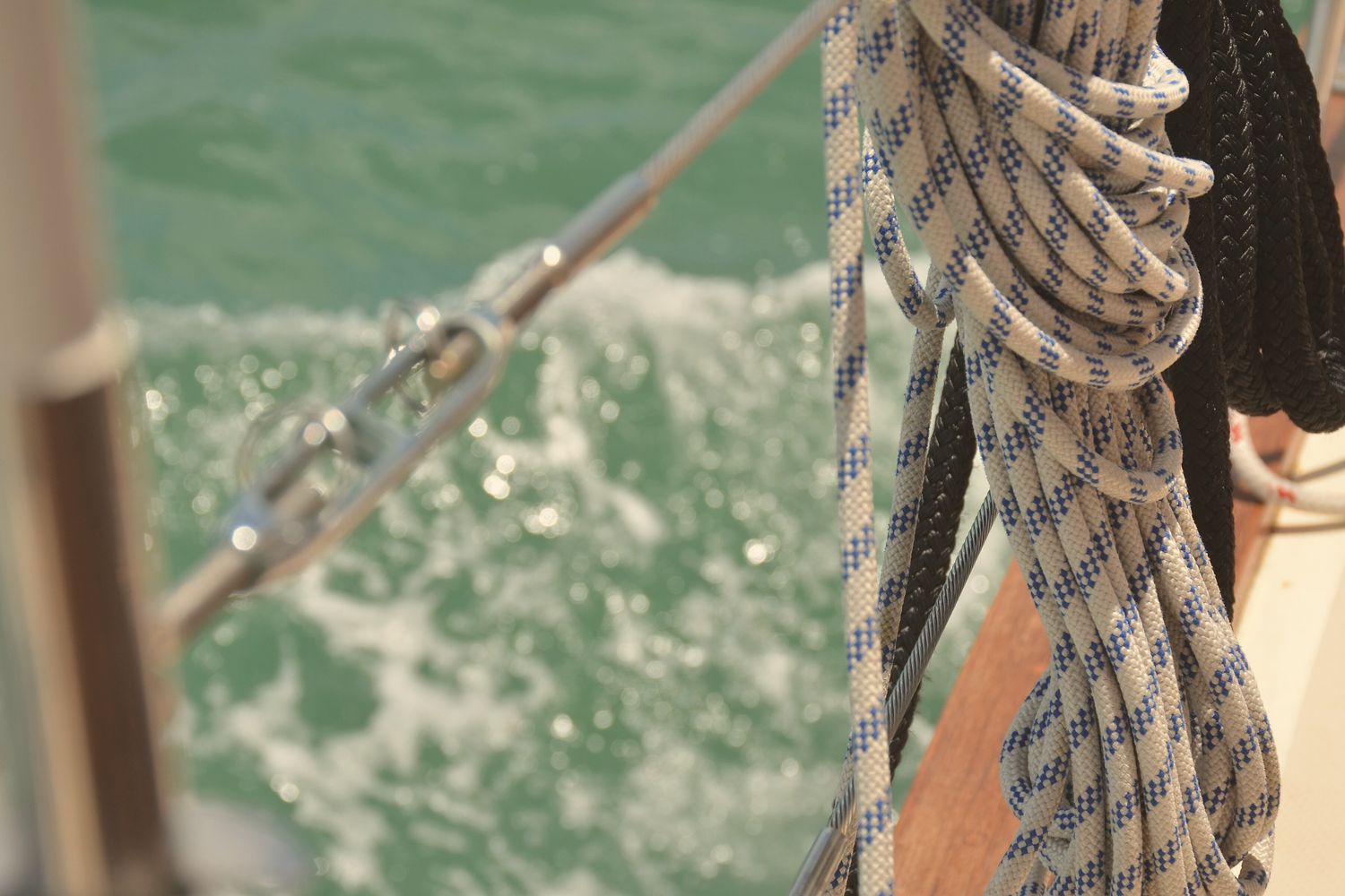 Coiled ropes and a shackle on a boat over green wake water.